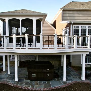 Elevated screen porch with deck railing, spiral stairs, and patio below