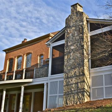 Screen porch addition with tall stone chimney on brick home