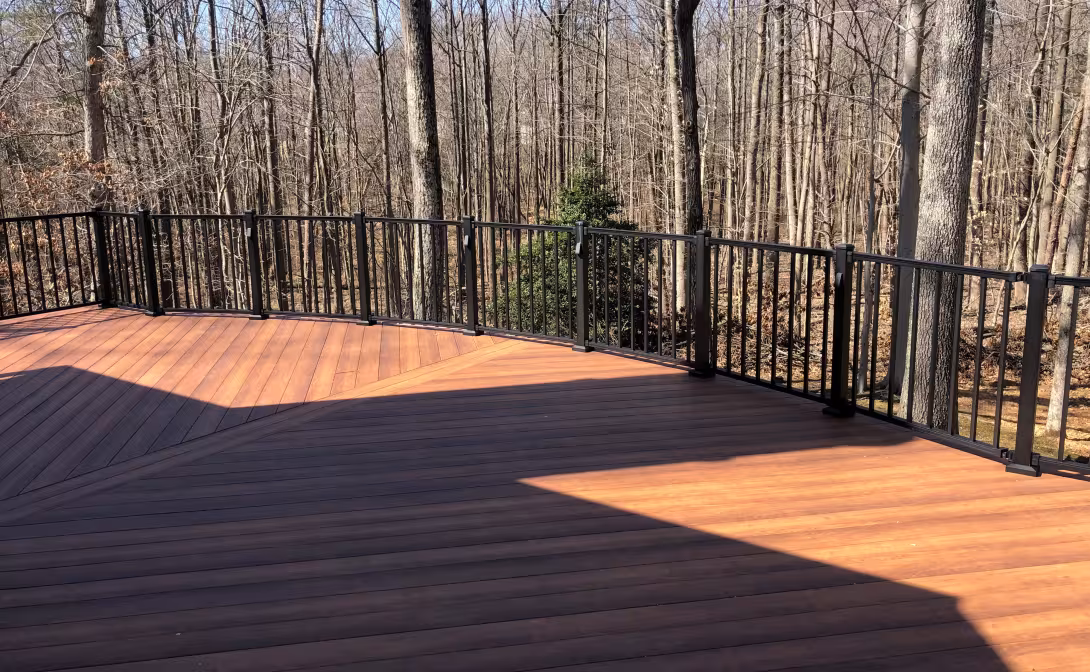 Curved wood deck with black railing overlooking leafless wooded yard